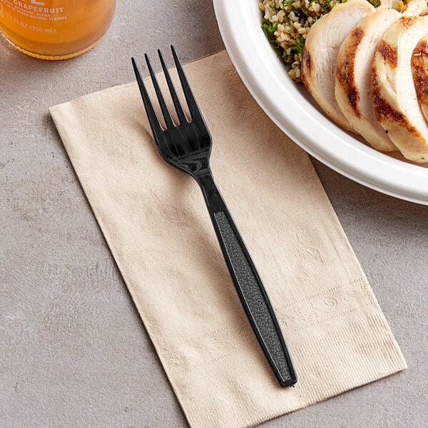 A black plastic Visions fork on a napkin next to a piece of meat.