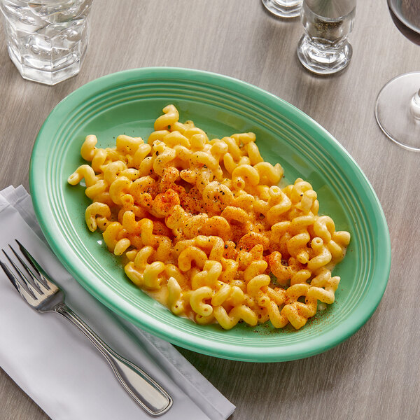 A Tuxton Cilantro oval china platter with a plate of macaroni and cheese and a fork.
