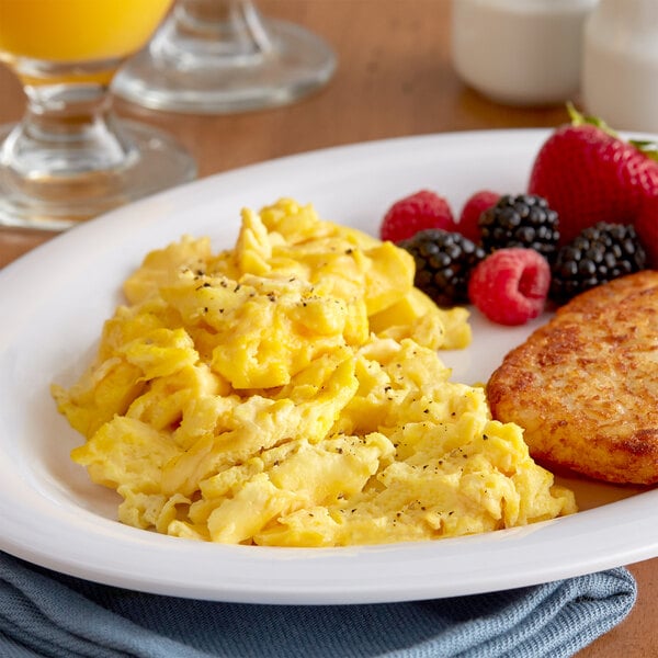 A white plate with scrambled eggs, fruit, and toast with a glass of juice on the side.
