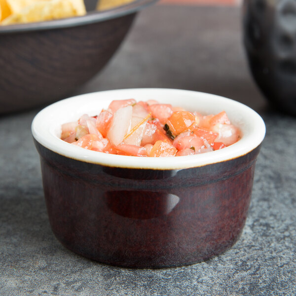 A Tuxton caramel and eggshell ramekin filled with salsa next to a bowl of chips on a table.