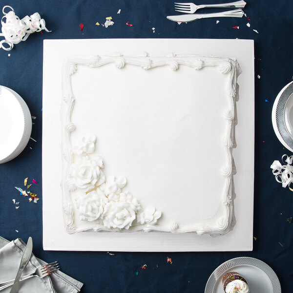 A white square cake on a white cake board with frosting flowers.