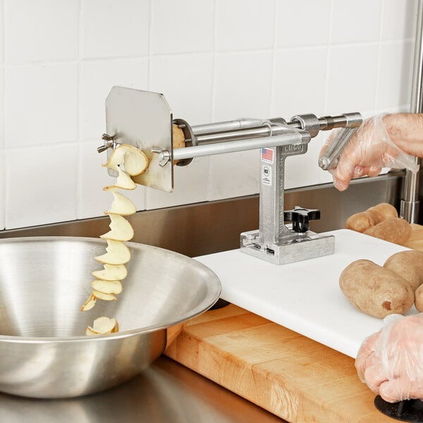 A person using a Nemco Straight Chip Twister Cutter to cut potatoes on a table.