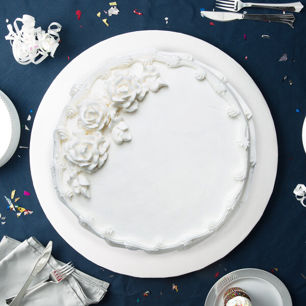 A white Enjay round cake drum under a white cake with white frosting and flowers on top.