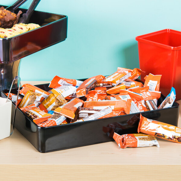 A black rectangular deli crock full of candy on a table.