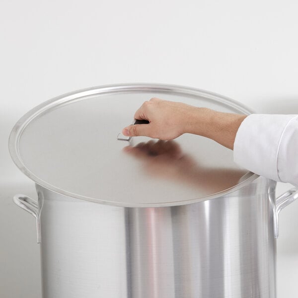 A hand using a Vollrath Wear-Ever aluminum pot cover on a large silver pot.