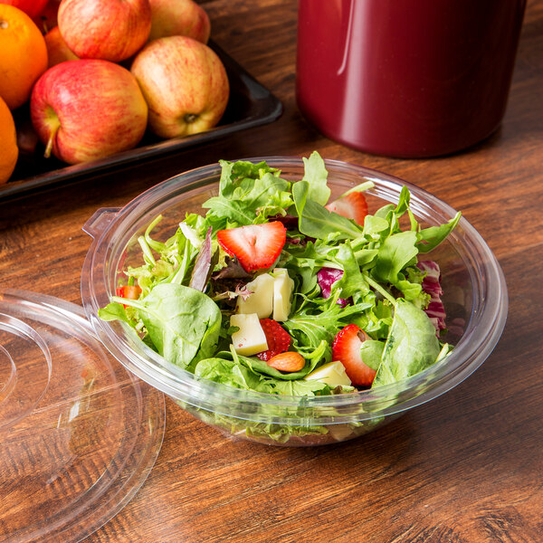 A clear plastic bowl of salad with green leaf lettuce, strawberries, cheese, apples, and oranges.