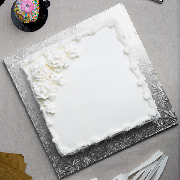 A white cake with frosting and flowers on a silver Enjay square cake drum.
