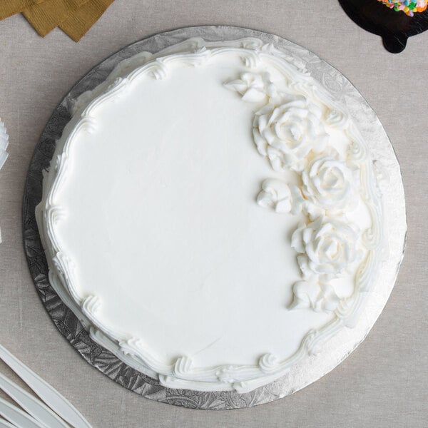 A white cake with frosting on a silver round cake board on a white table.