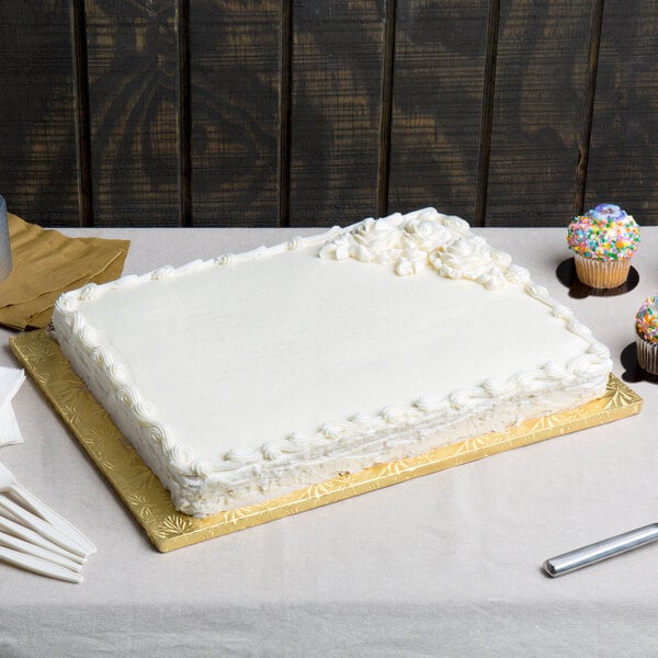 A white cake with frosting on a gold Enjay half sheet cake board on a table.