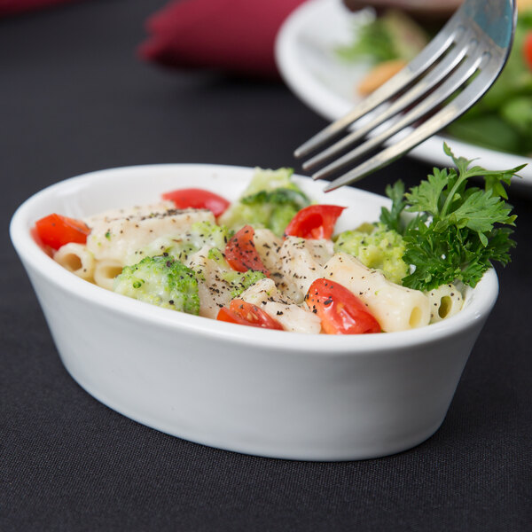 A fork holding pasta and vegetables in a white Tuxton oval baker.
