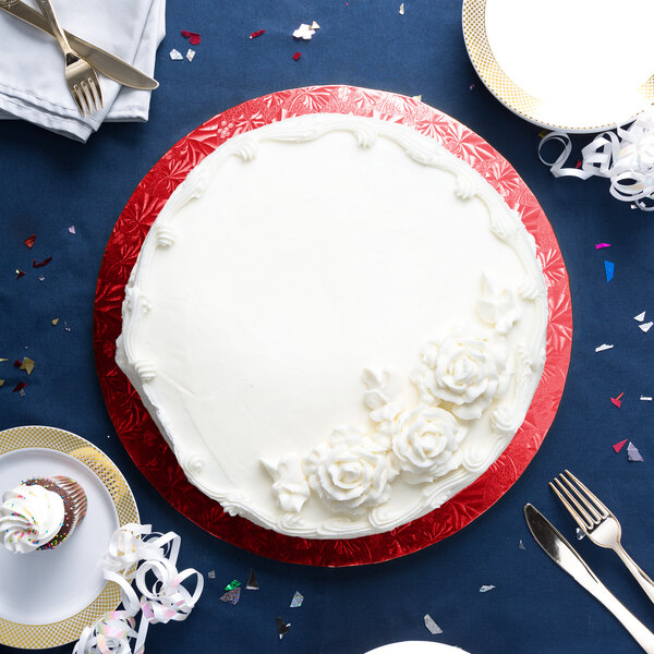 A white cake with white frosting on a red Enjay cake drum on a blue table with silverware.