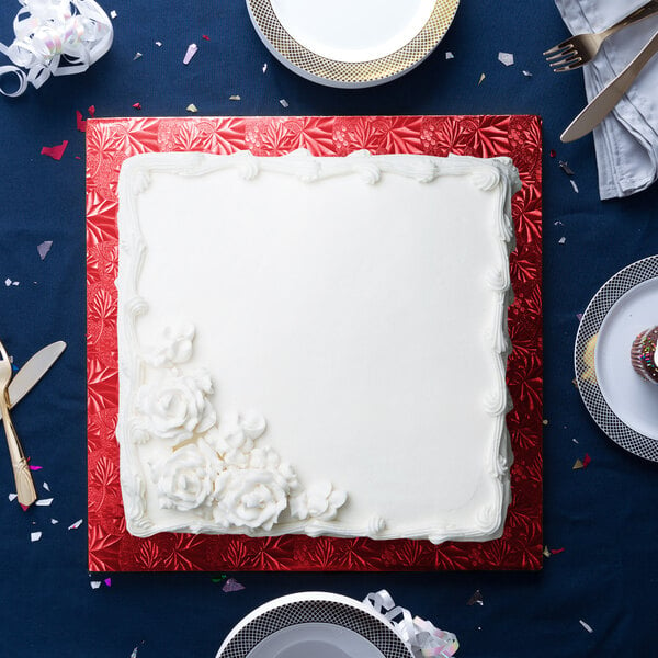 A white square cake on a red Enjay cake board with white flowers.