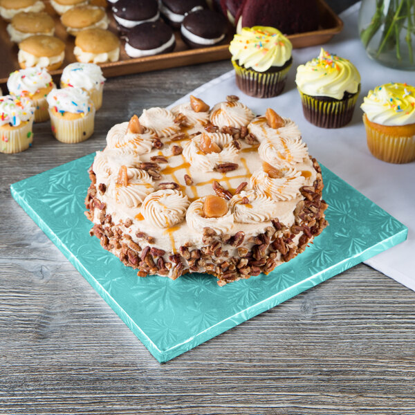 A cake with frosting and pecans sits on a blue Enjay cake board on a table.