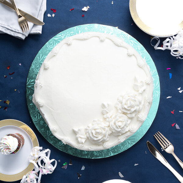 A white frosted cake on a blue Enjay cake board with silverware.