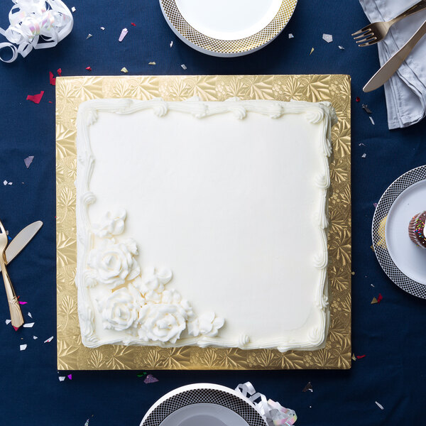 A white square cake with white frosting and flowers on a gold Enjay square cake drum.