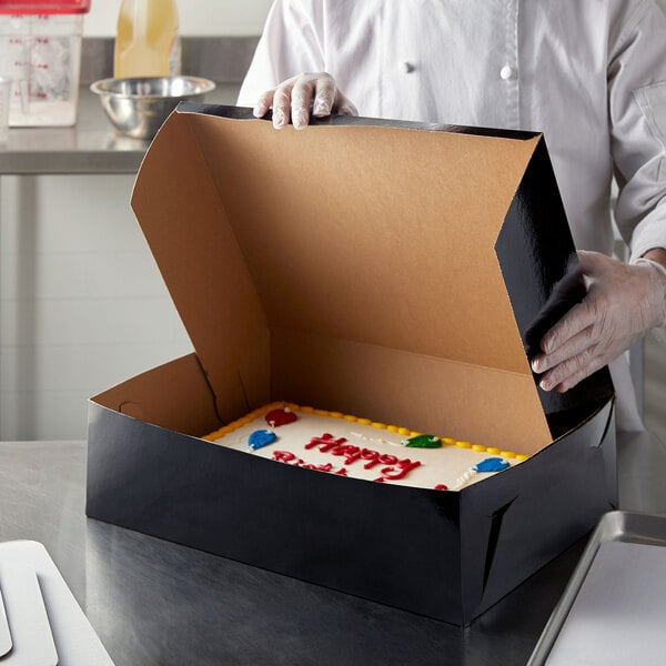A chef opening a black Enjay half sheet cake box to reveal a cake.