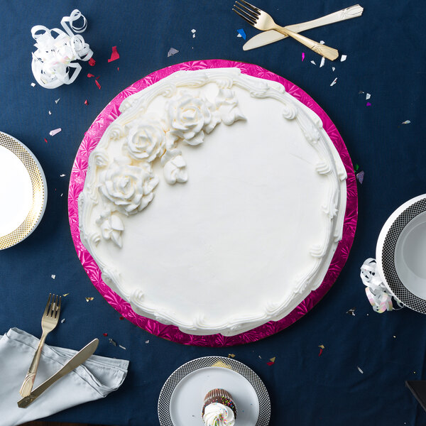 A cake with white frosting on a pink Enjay cake drum on a blue table.