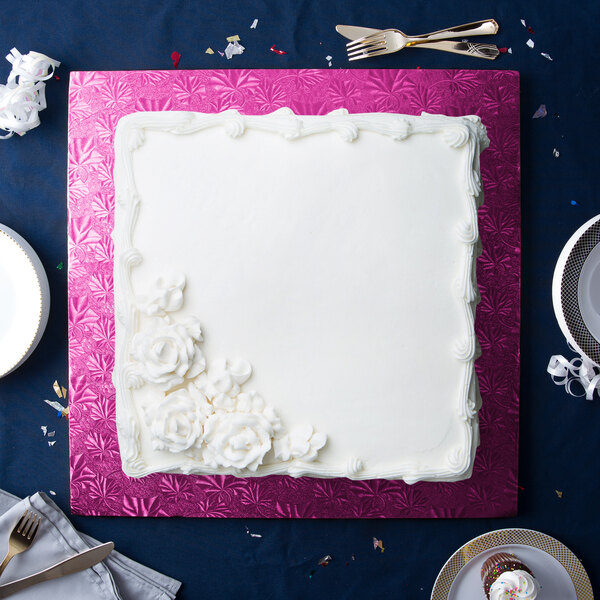 A white square cake on a pink Enjay cake board with white flowers on top.