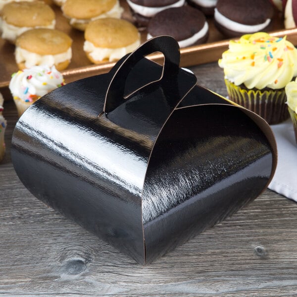 A black Enjay cupcake box with a handle next to cupcakes.