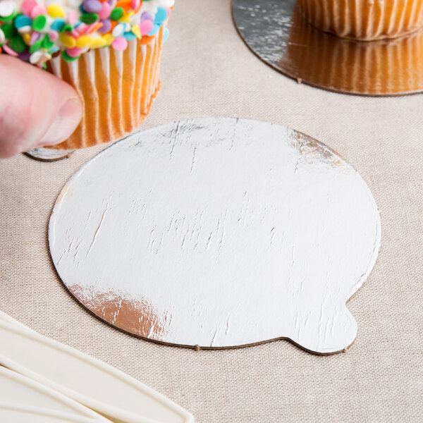 A finger holding a cupcake with sprinkles on a silver and gold reversible round single serve dessert board.