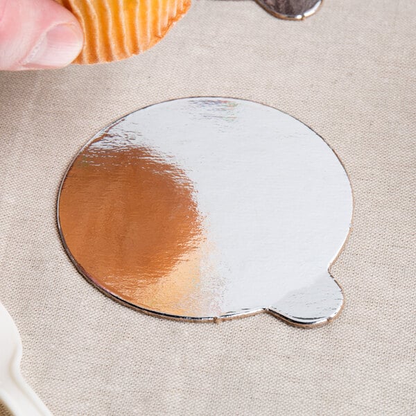 A person holding a cupcake on a silver and gold reversible round dessert board with a tab.