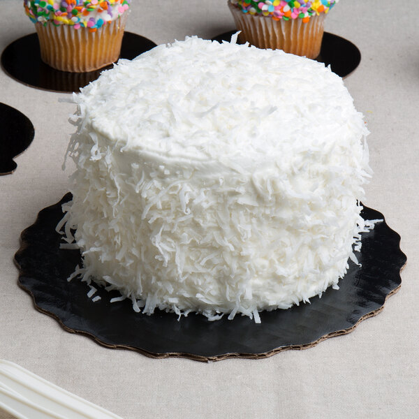 An Enjay black laminated corrugated cake circle with a white cake and cupcakes with white frosting.