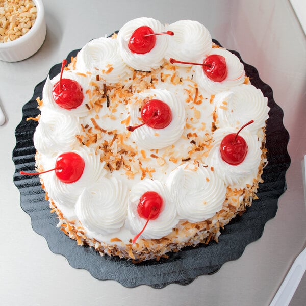 A cake with white frosting and red cherries on a black Enjay cake circle.