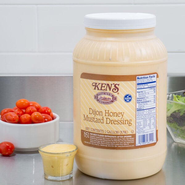 A container of Ken's Foods Dijon honey mustard dressing next to a bowl of cherry tomatoes.