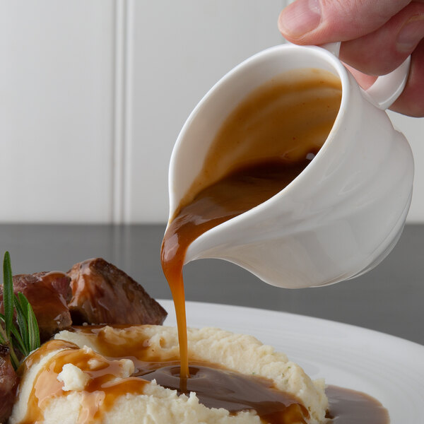 A person pouring Trio brown gravy onto a plate of mashed potatoes.