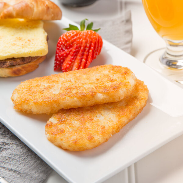 A plate of Ore-Ida hash brown patties with a breakfast sandwich and a strawberry on the side.