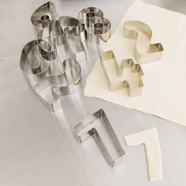 A set of Ateco stainless steel number cookie cutters on a white surface.