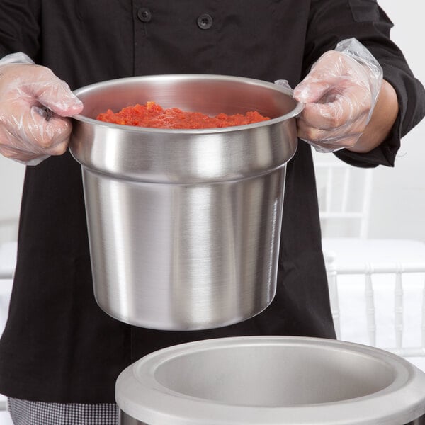 A person holding a 7 Qt. stainless steel inset filled with red sauce.