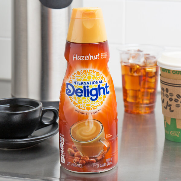 A cup of coffee with a bottle of International Delight Hazelnut Coffee Creamer on a counter.