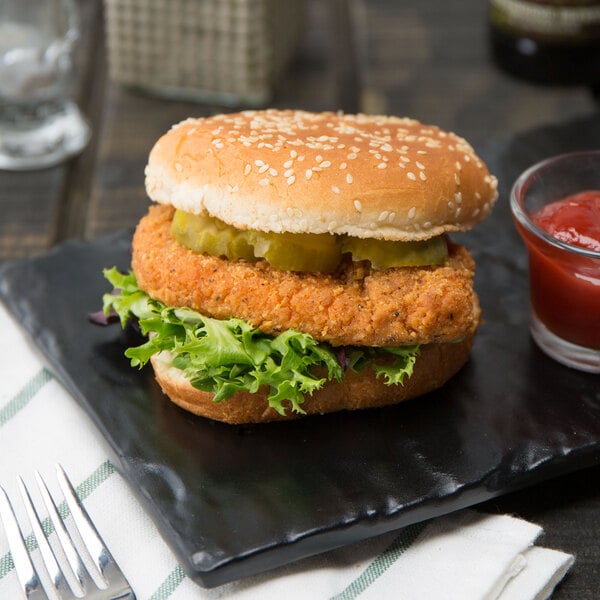 A black plate with a chicken sandwich with pickles and ketchup.