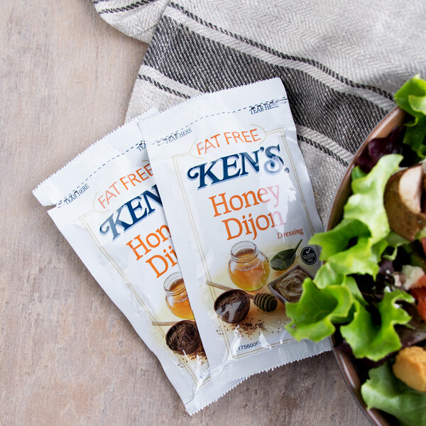 A bowl of salad with Ken's Fat-Free Dijon Honey Mustard dressing packets on the side.