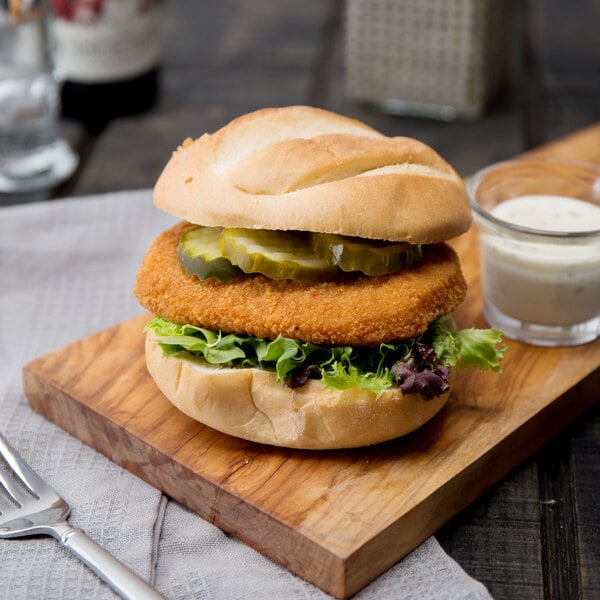 A chicken sandwich with pickles and lettuce on a wooden board.