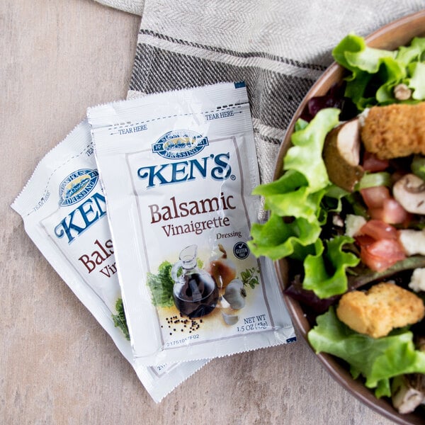 A bowl of salad with two Ken's Balsamic Vinaigrette packets on the side.