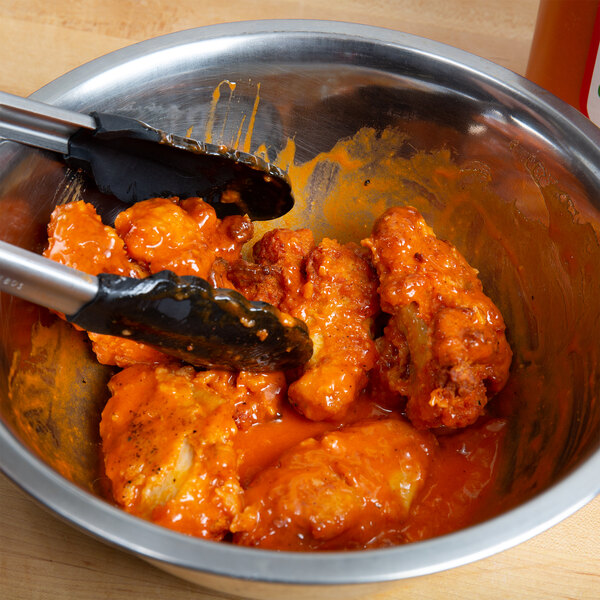 A bowl of buffalo wings with tongs being used to serve them.