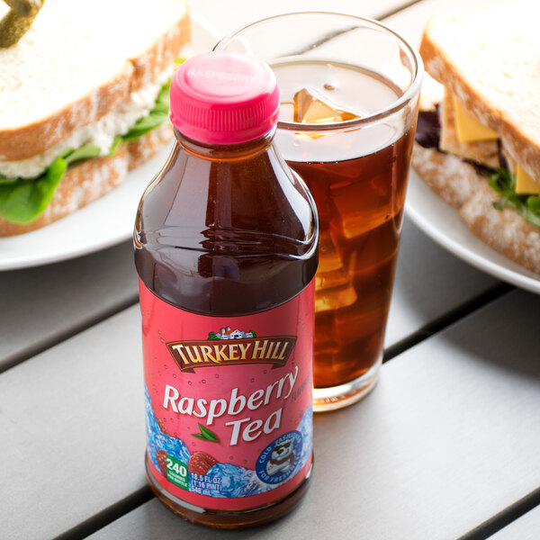 A bottle of Turkey Hill raspberry iced tea on a table next to a sandwich.