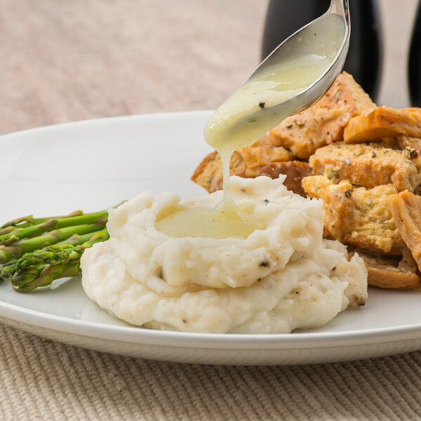 A plate of mashed potatoes and asparagus with Trio chicken gravy poured over it on a white background.