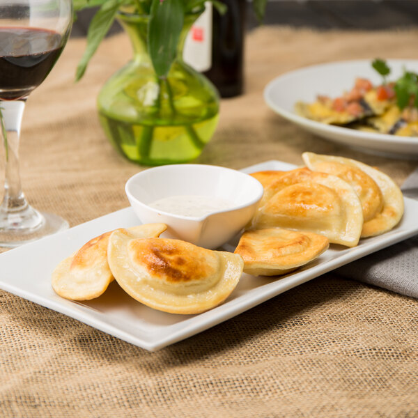 A plate of Mrs. T's Classic Cheddar Potato Pierogies with a bowl of sauce on a table.