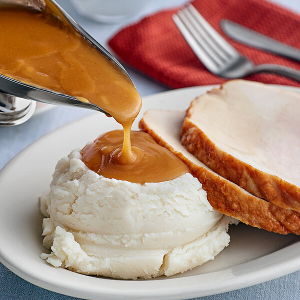 A plate with turkey, mashed potatoes, and LeGout turkey gravy being poured over them.
