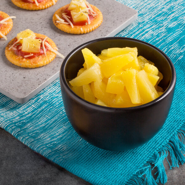 A bowl of pineapple tidbits next to cheese and crackers.