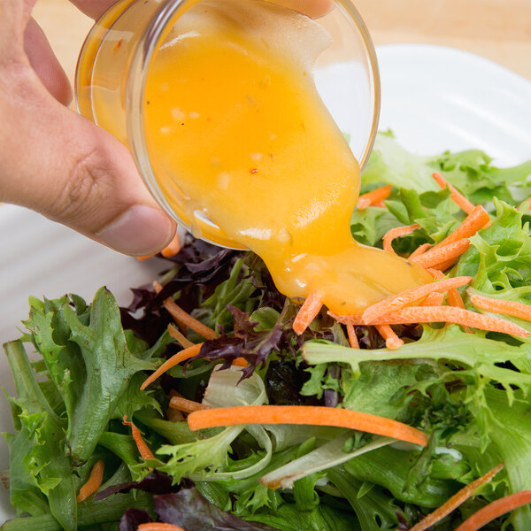 A hand pouring Ken's Foods Golden Italian Dressing over a bowl of salad.