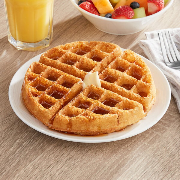 A waffle on a plate with a bowl of fruit and a glass of orange juice.