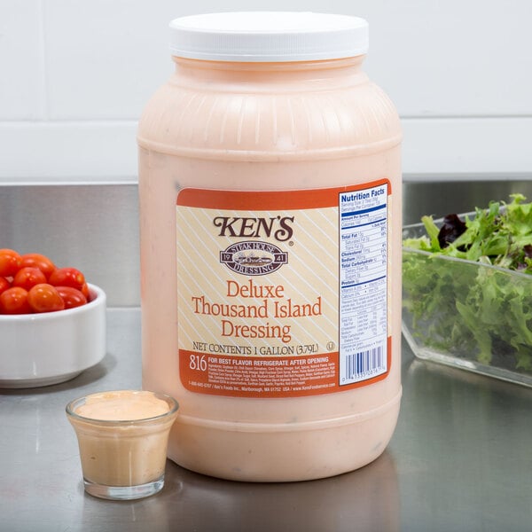 A case of Ken's Foods Deluxe Thousand Island Dressing on a table next to a bowl of salad.