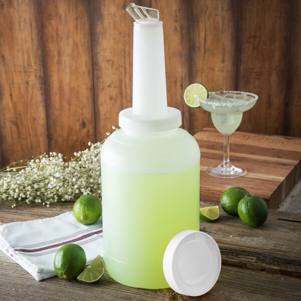 A Carlisle white container of limeade with a lime wedge next to a glass of margarita.