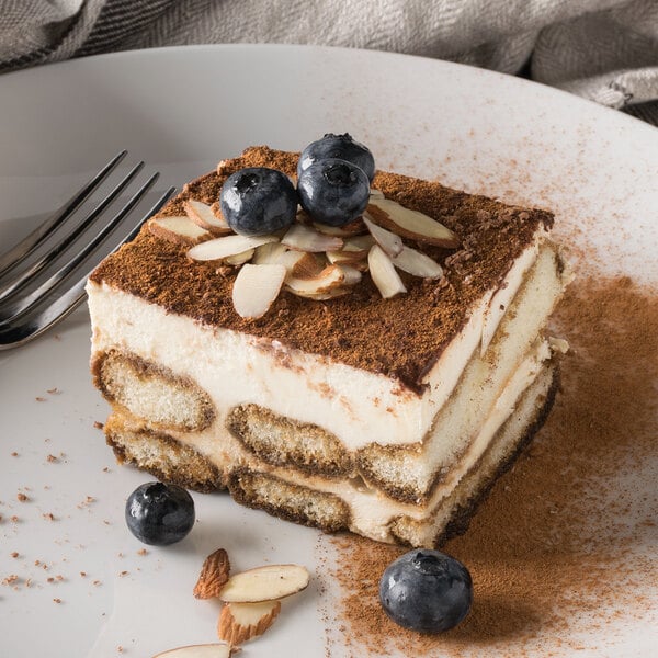 A slice of tiramisu cake with blueberries and almonds on a white plate.