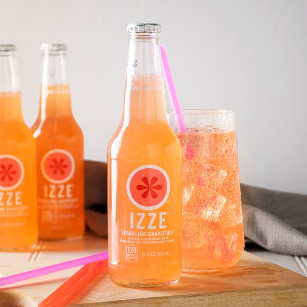 A group of Izze sparkling grapefruit juice bottles and a glass of grapefruit juice.