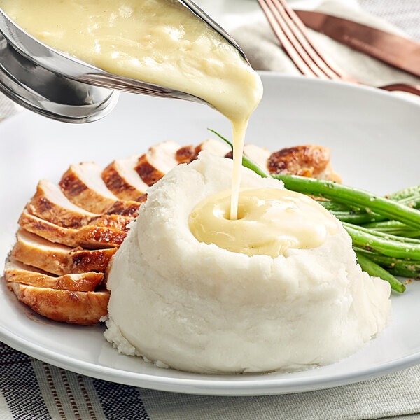 A plate of mashed potatoes and green beans with LeGout chicken gravy being poured over it.